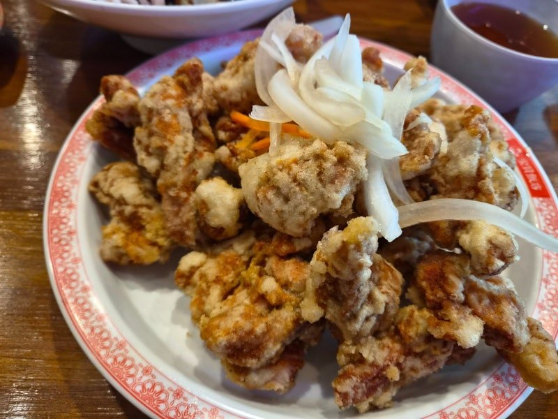 A plate of Korean sweet and sour pork at Bobae Banjeom, pale crisp battered pieces topped with raw onion slices and shredded carrot. The sauce is not poured over it.
