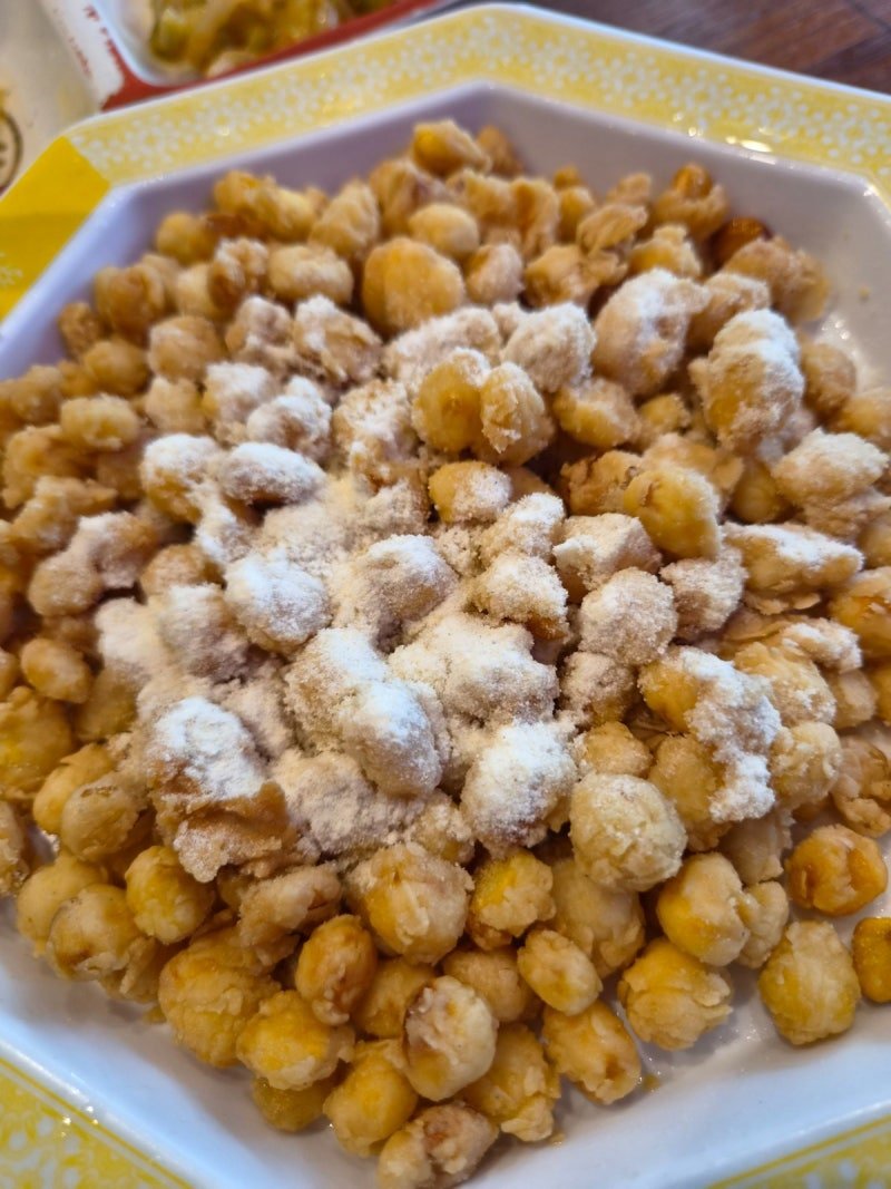 Deep-fried corn kernels dusted with pale consomme seasoning powder, served on a white octagonal plate with a yellow rim.