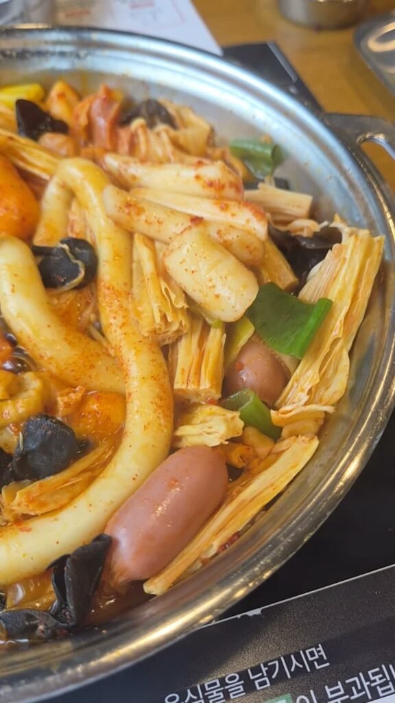 A finished pot of tteokbokki at Dookki, red with rice cakes, sausages and wood ear mushrooms