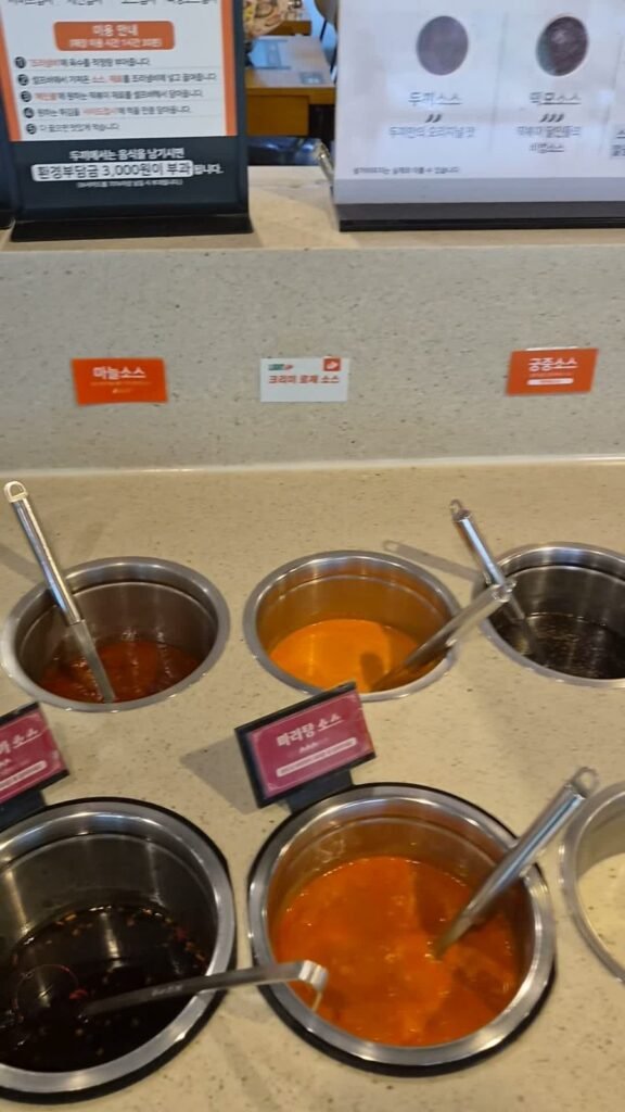 The sauce self bar at Dookki with labelled pots of different tteokbokki sauces and ladles