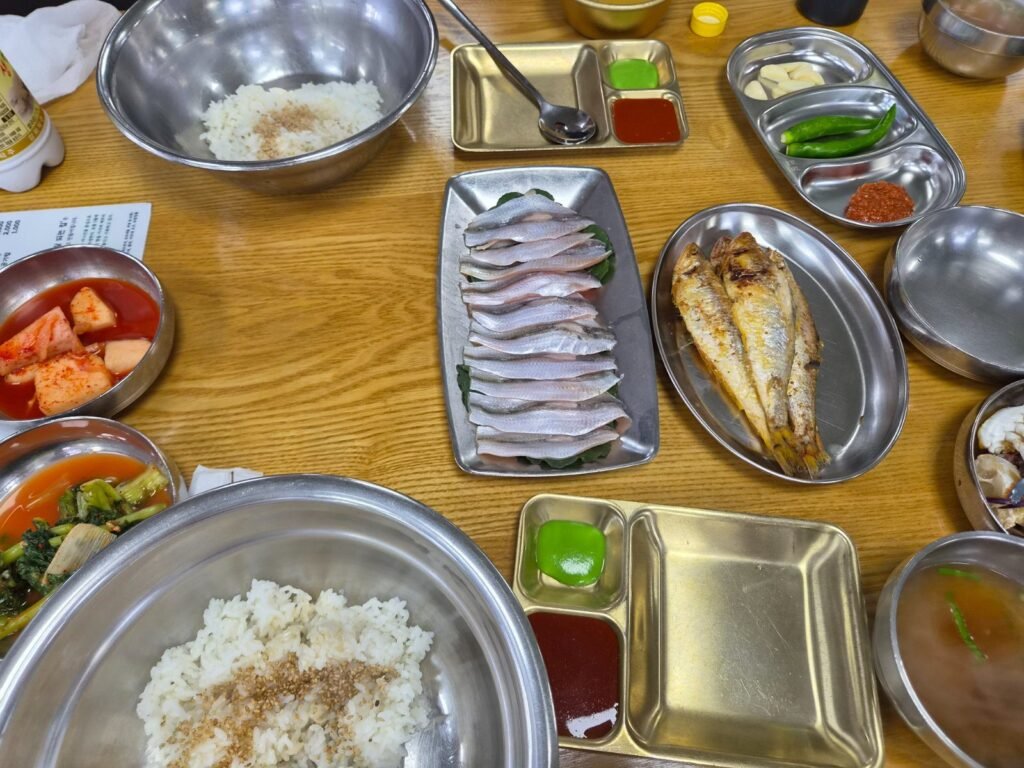 A bandaengi meal on Ganghwa Island: thin slices of raw fish, a whole grilled fish, rice, red soup and metal bowls of side dishes