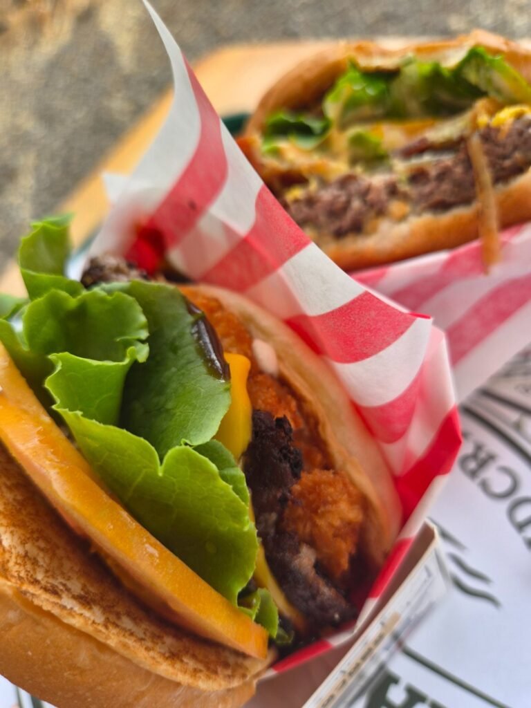 Close-up of a burger at Masian 300 with a thick beef patty, melted cheddar and lettuce in a red striped paper wrap