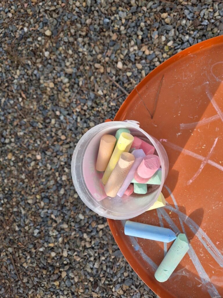 A cup of coloured chalk on an outdoor table on the gravel yard at Masian 300