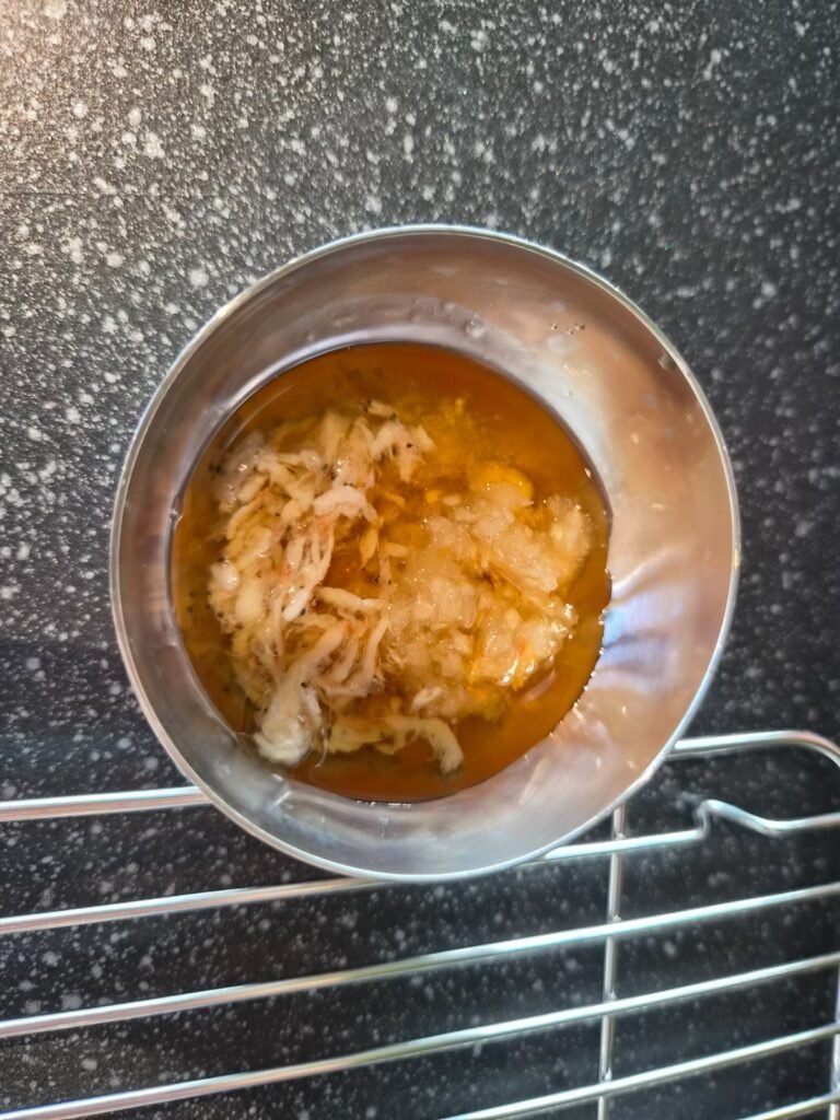 A small metal bowl of the house dipping sauce sitting on the grill at Naengsamdo, used for dipping cooked pork