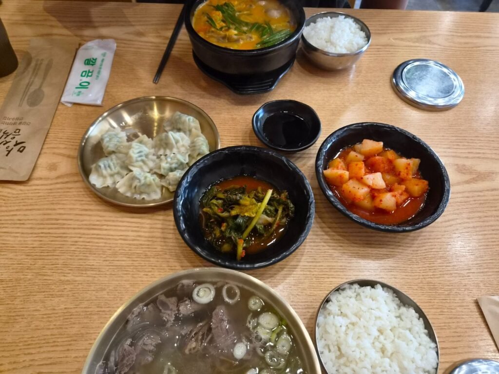 A full table at Unseook: clear gomtang, spicy pork gukbap, water dumplings, kimchi and rice