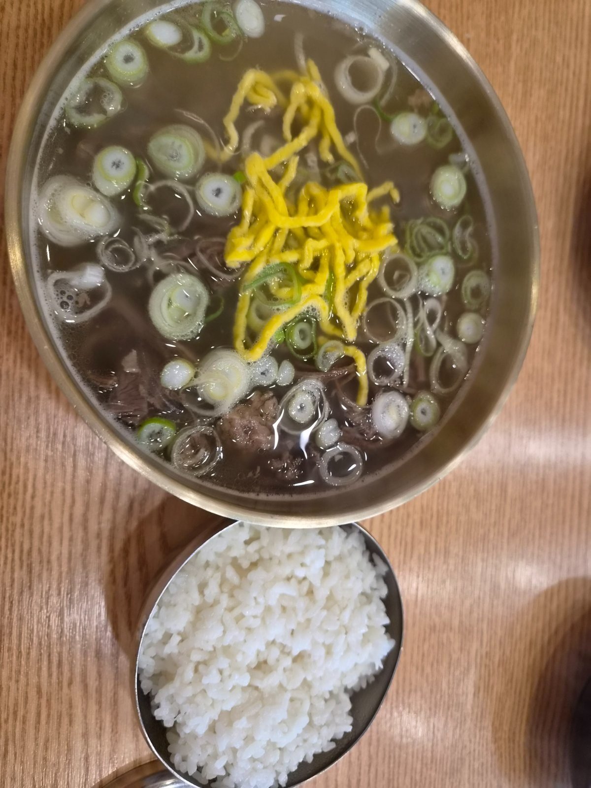 Clear Naju gomtang beef broth topped with spring onion and shredded egg, served with a bowl of rice