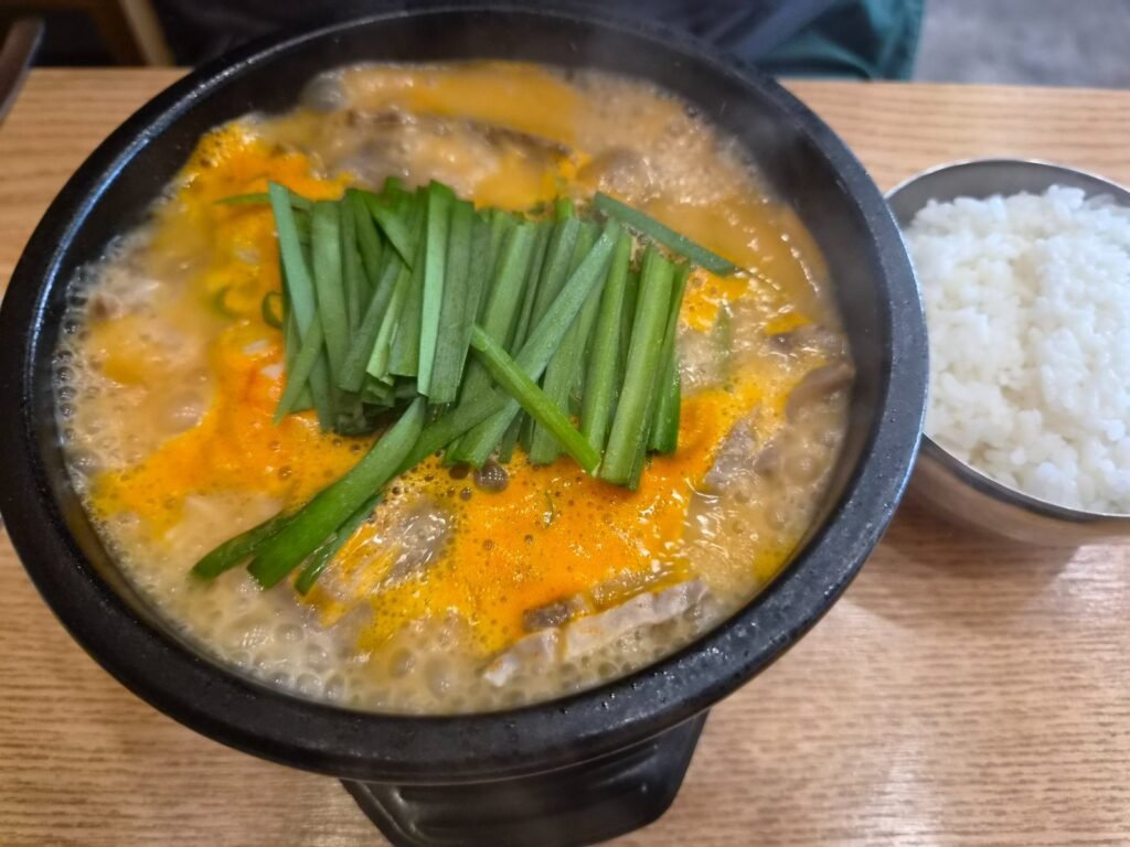 Spicy eolkeun pork gukbap in a stone bowl topped with garlic chives, served with rice