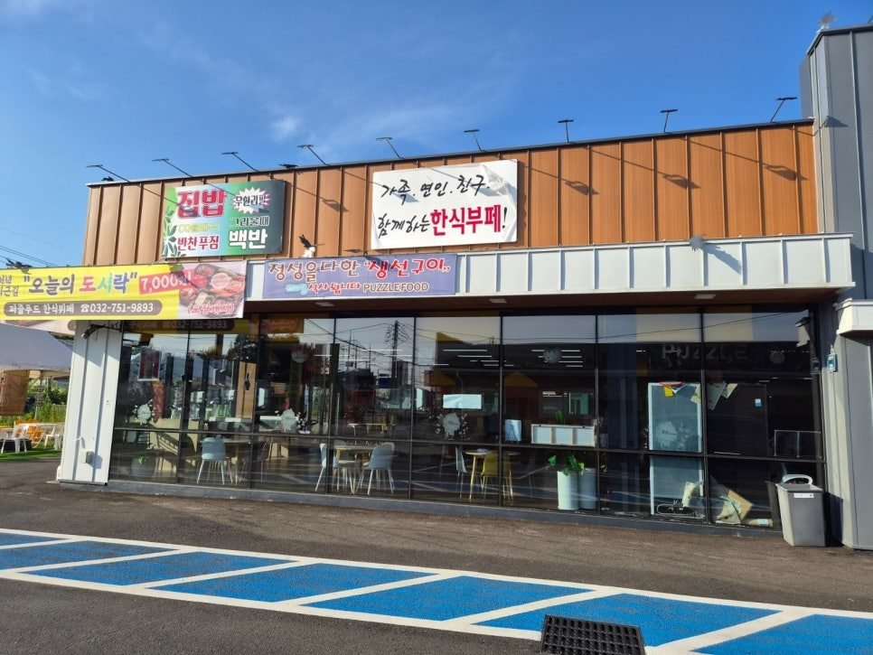 Orange-panelled single-storey restaurant with a glass front and a blue-striped car park, Korean signs reading 집밥 백반 반찬무한 and 한식부페 above the entrance