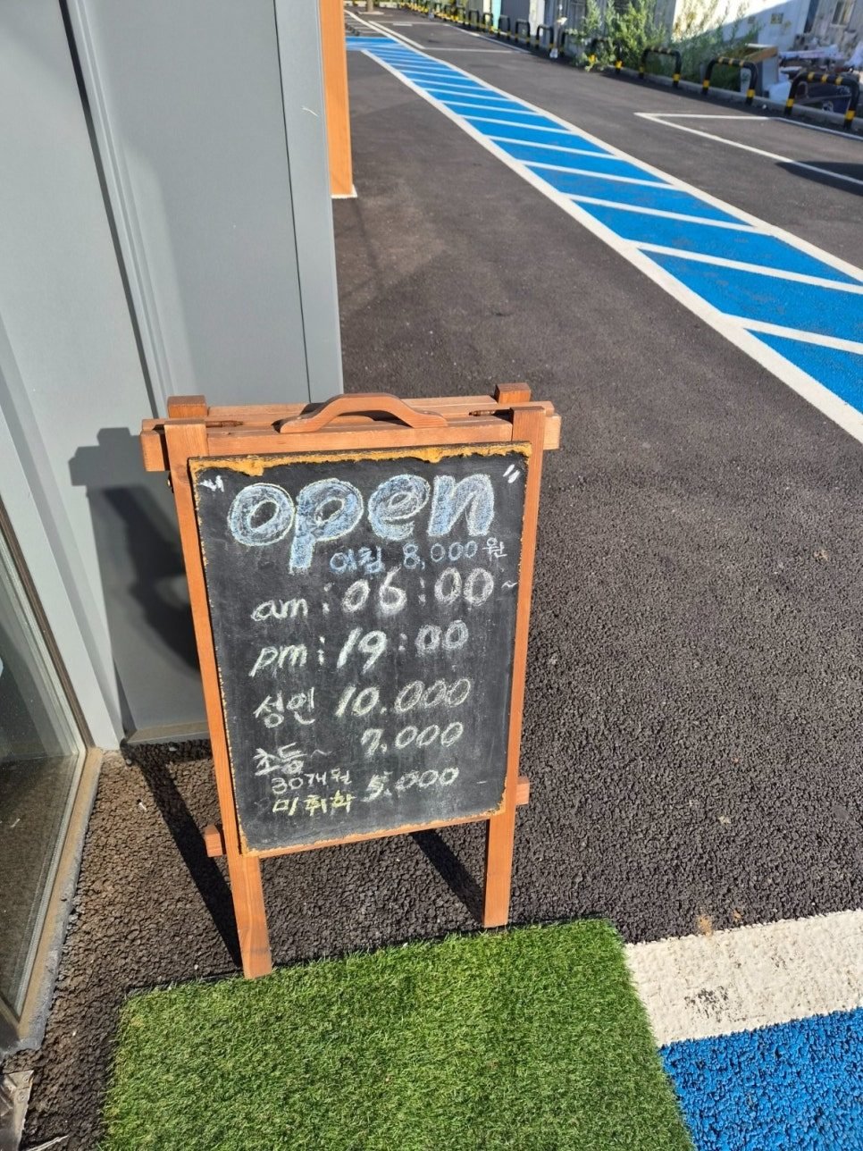 Wooden A-frame chalkboard reading open, 아침 8,000원, am 06:00, pm 19:00, 성인 10,000, 초등 7,000, 미취학 5,000