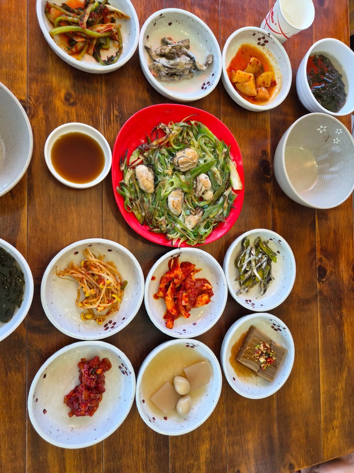 Wooden table set with grilled fish meal side dishes in white bowls, oyster pancake on a red plate in the centre