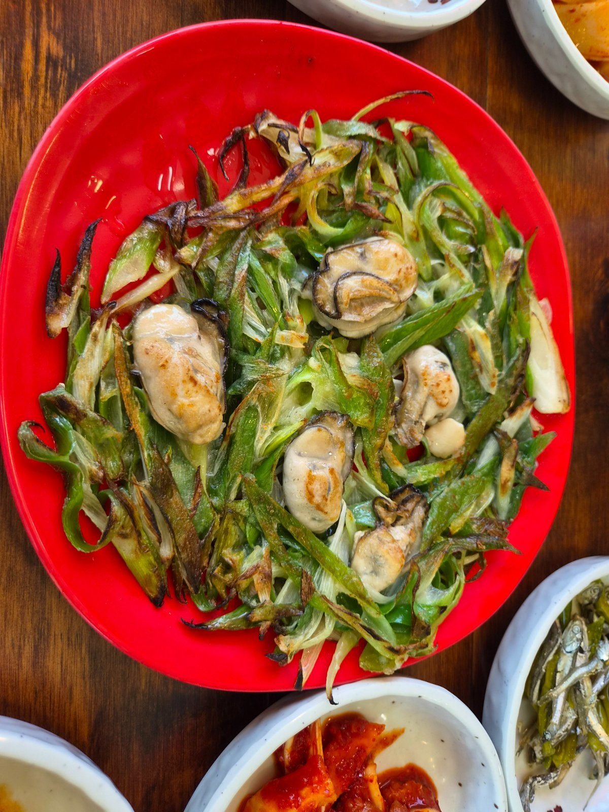 Oyster pancake on a red plate, whole oysters set into a bed of fried spring onion