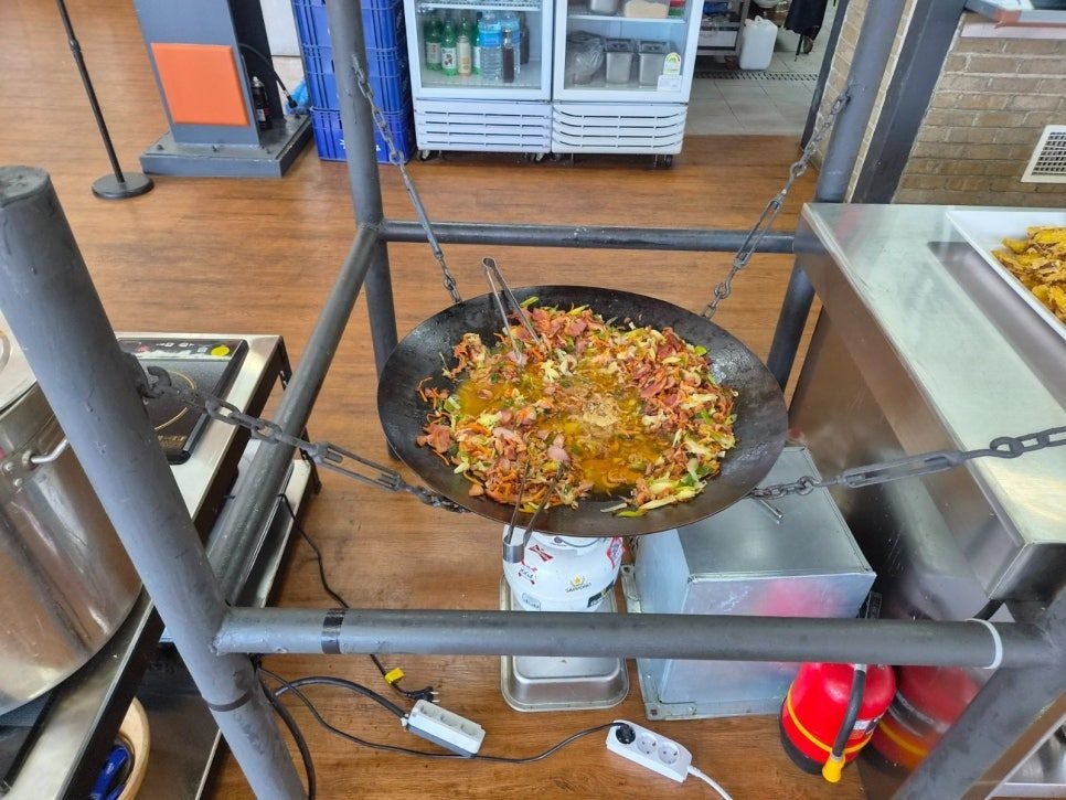 Large cast-iron cauldron suspended over a burner holding smoked duck stir-fried with cabbage and vegetables