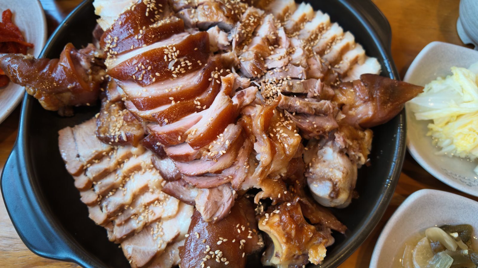 The jokbal and bossam set, sliced braised pork and boiled pork piled on a black platter with sesame seeds