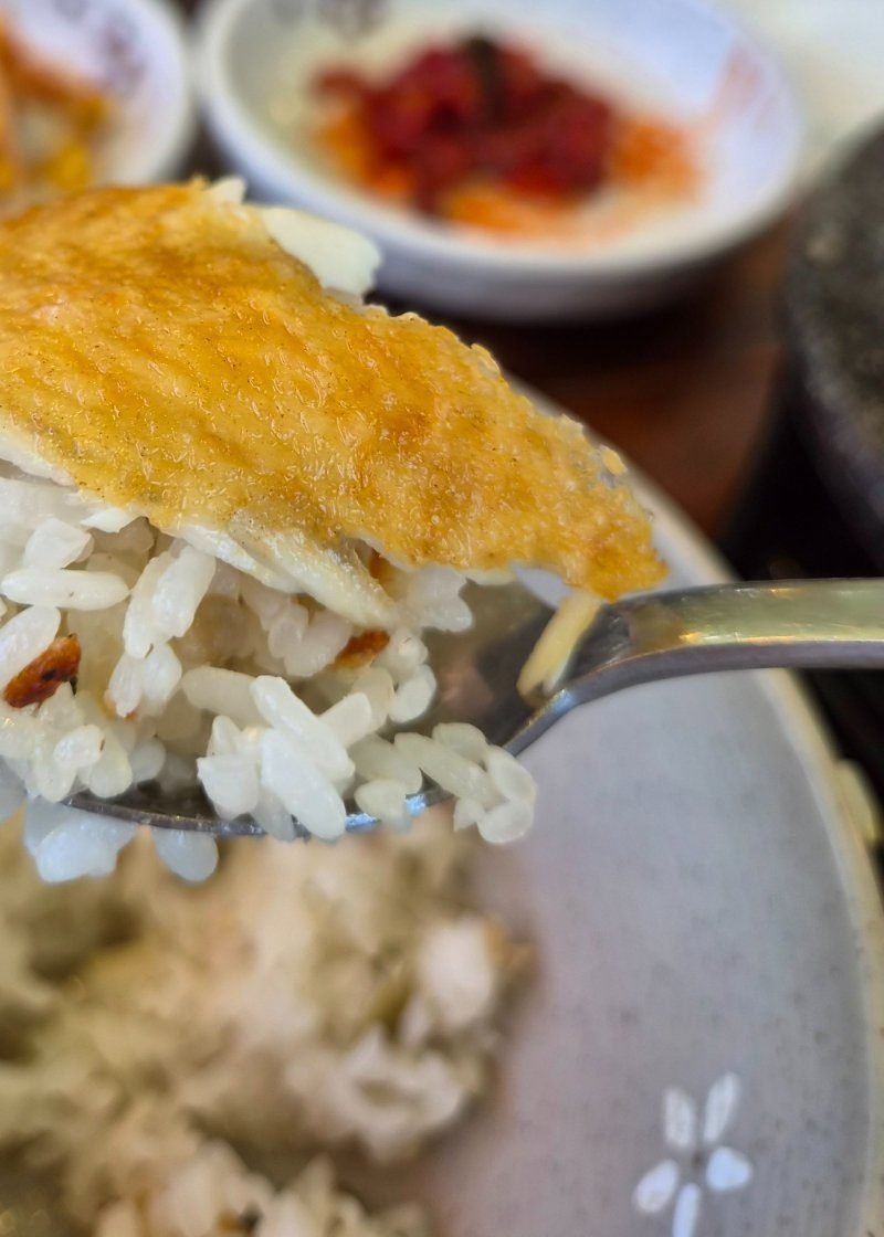 Spoonful of stone pot rice topped with a piece of grilled fish, the stone bowl below