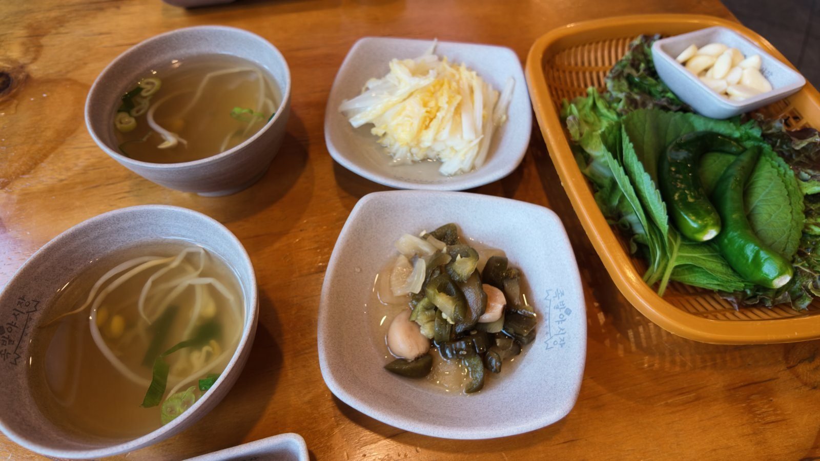 Free side dishes: bean sprout soup, pickled radish, pickled peppers and a basket of lettuce and perilla leaves