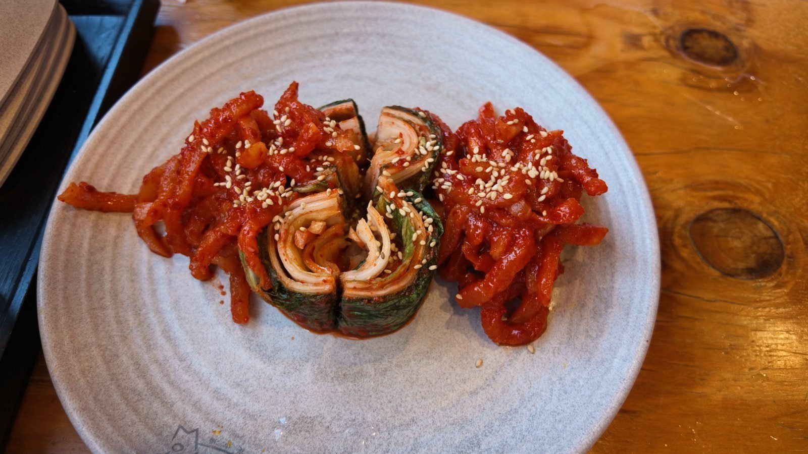 Bossam kimchi rolled into cylinders on a plate beside seasoned radish salad