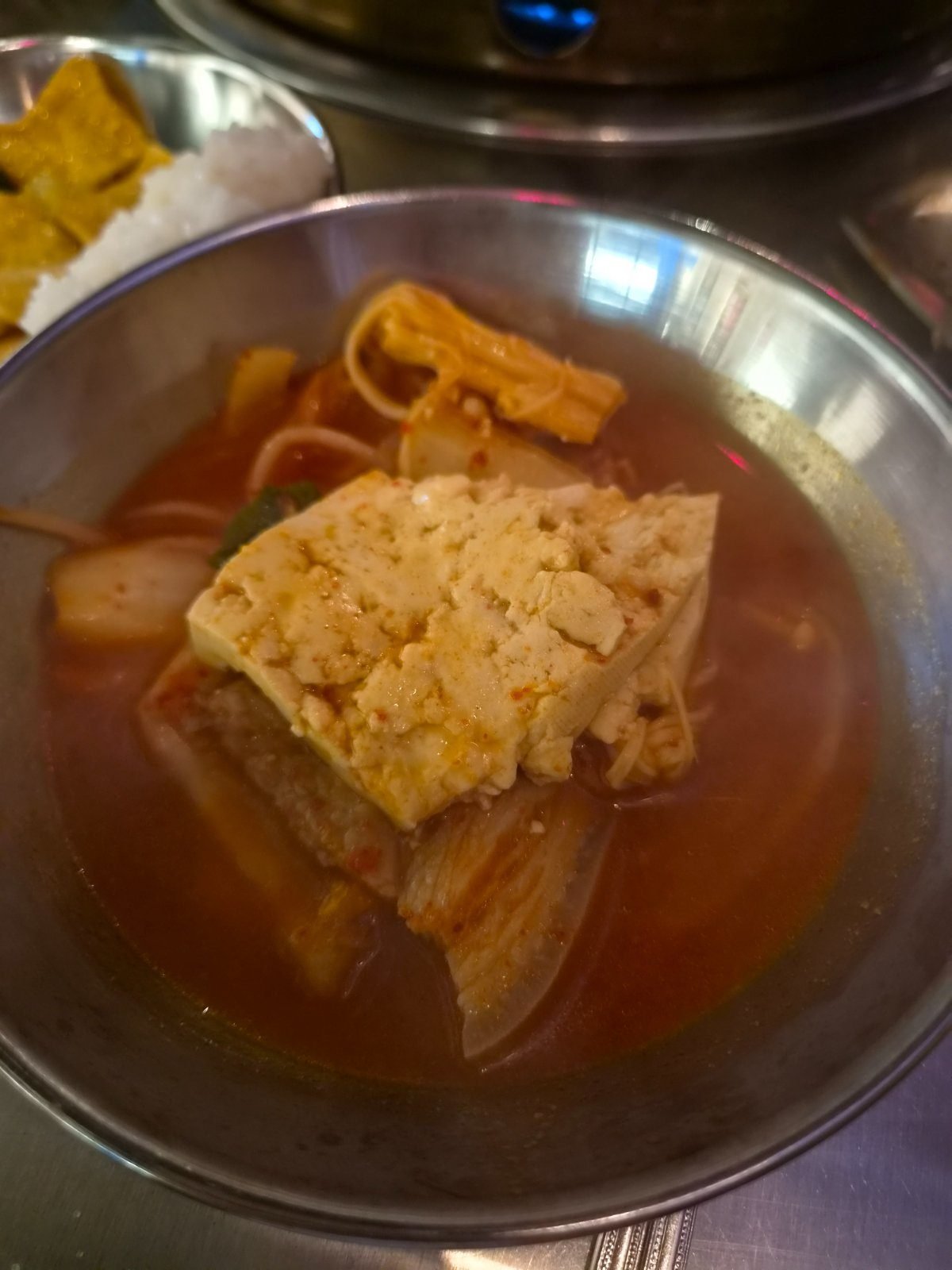 A thick slab of tofu sitting on aged kimchi in the red kimchi stew broth