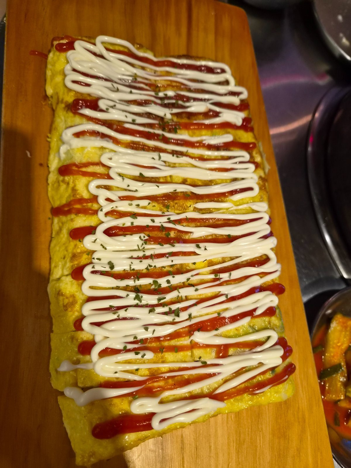 A long rolled omelette on a wooden board, striped with ketchup and mayonnaise