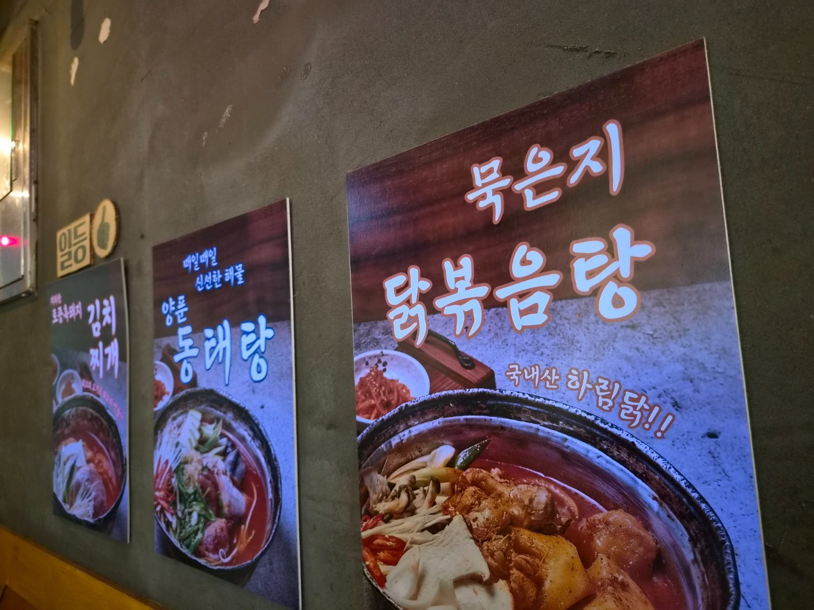 Three large photo signs on the restaurant wall for kimchi stew, pollack stew and spicy braised chicken