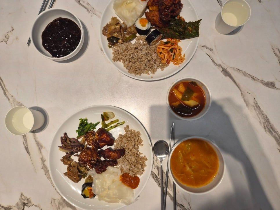 Two plates from the 9,900 won buffet at Bangatgan: barley rice, fried chicken in sweet-and-spicy sauce, mini gimbap, greens and side dishes, with a bowl of black-bean sauce and two bowls of soup.
