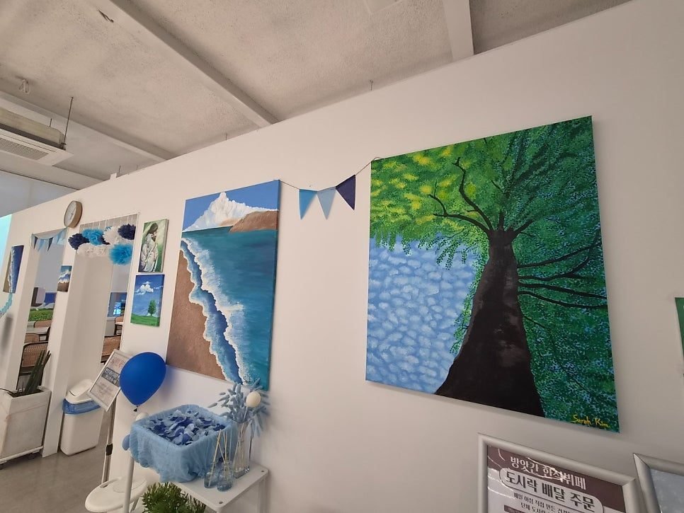 Two large canvases on the dining-room wall of Bangatgan, one of a tree and one of a shoreline, with smaller framed pieces further along the wall.