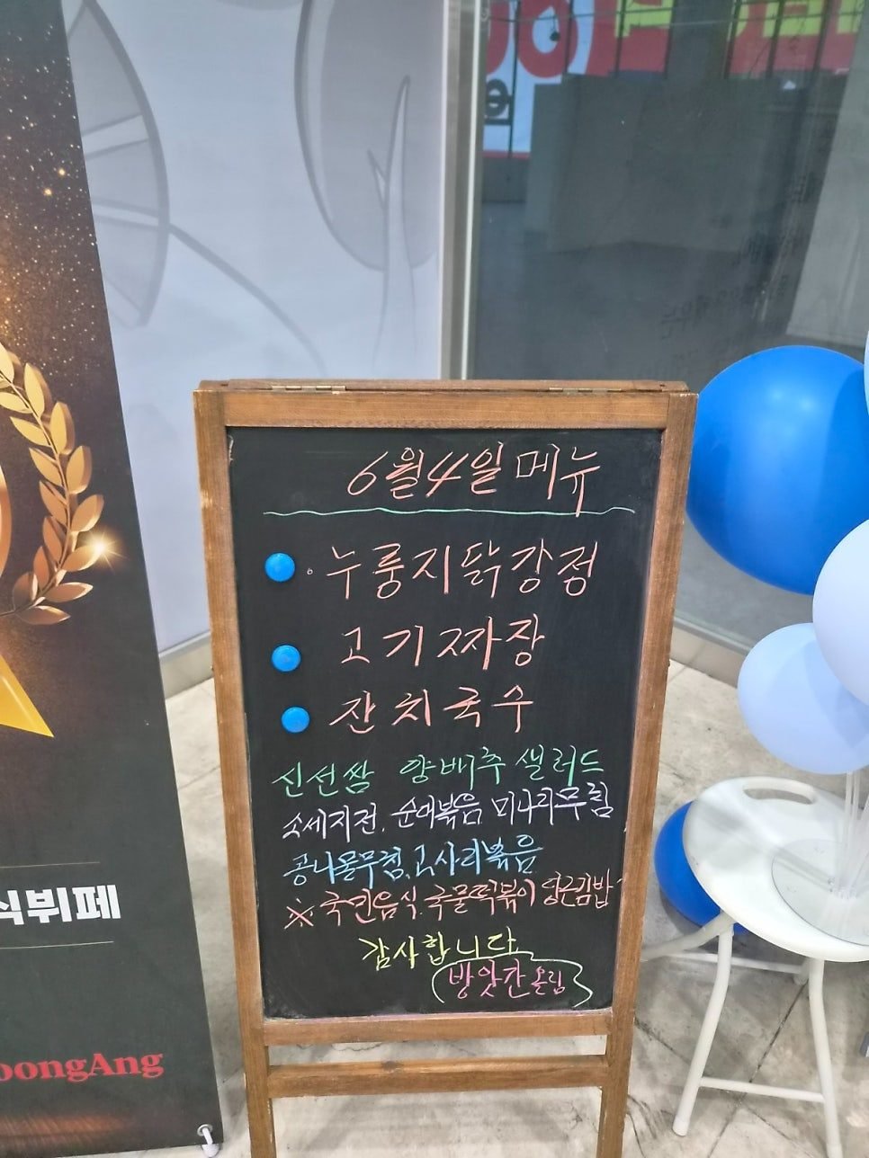A chalkboard at the entrance headed 6월 4일 메뉴, listing 누룽지닭강정, 고기짜장 and 잔치국수 as the day's main dishes.