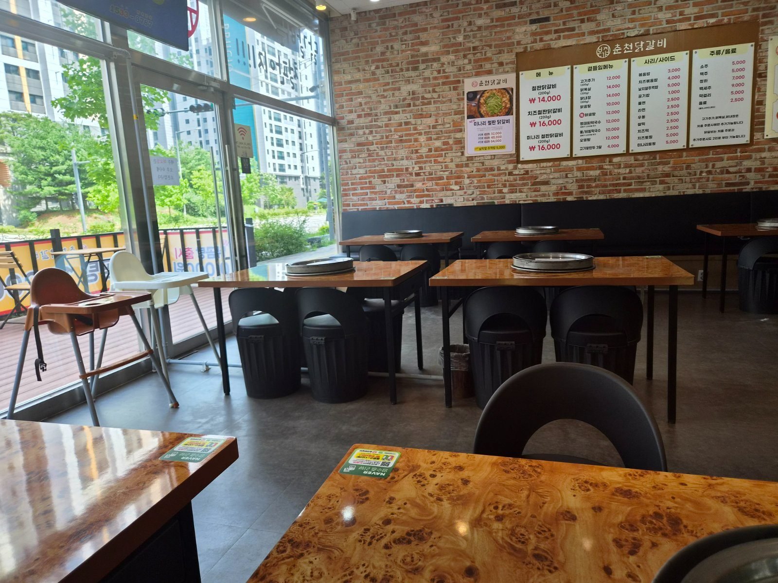Empty dining room with wooden tables, each with a round griddle set into the middle, chairs and floor-to-ceiling windows