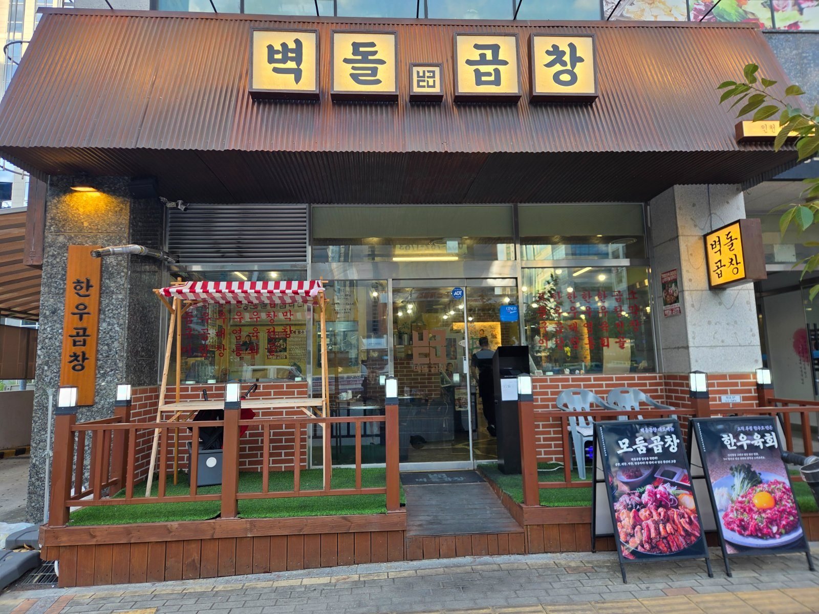 Orange sign reading 벽돌곱창 above a red brick storefront with a red and white striped canopy over a small wooden deck