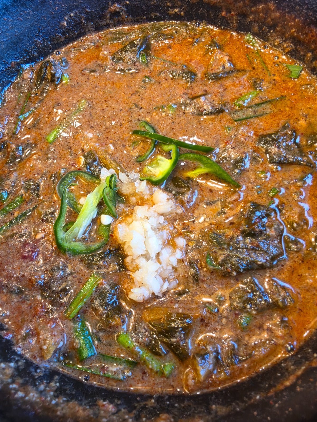 Bubbling stone pot of chueotang, a thick brown ground-loach and doenjang soup packed with dark siraegi greens, topped with sliced green cheongyang chilli and minced garlic
