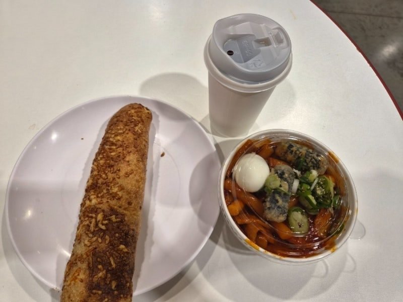 A bake, a bowl of tteokbokki and a lidded cup on a table