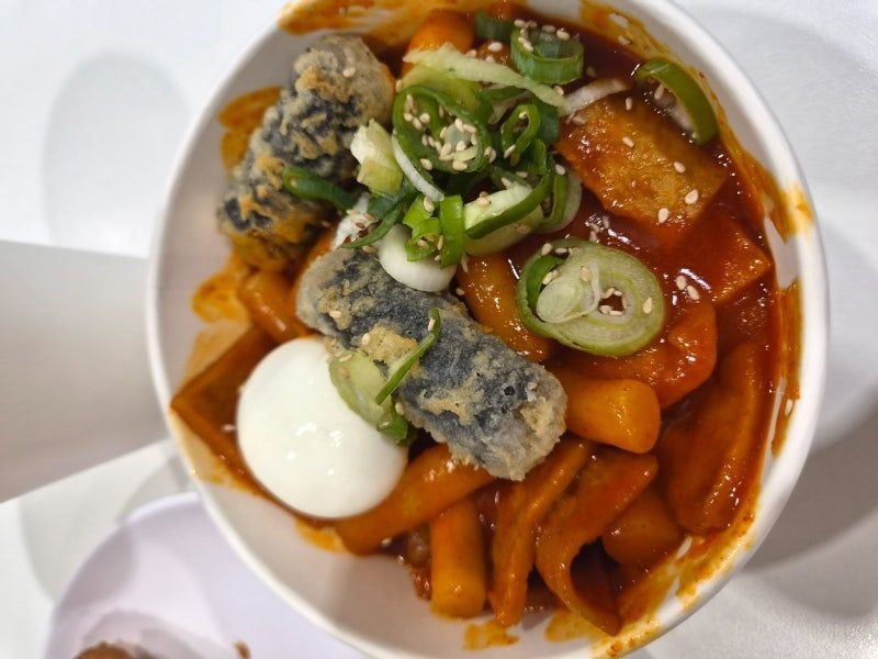 Tteokbokki topped with a boiled egg, fried seaweed rolls and sliced green onions