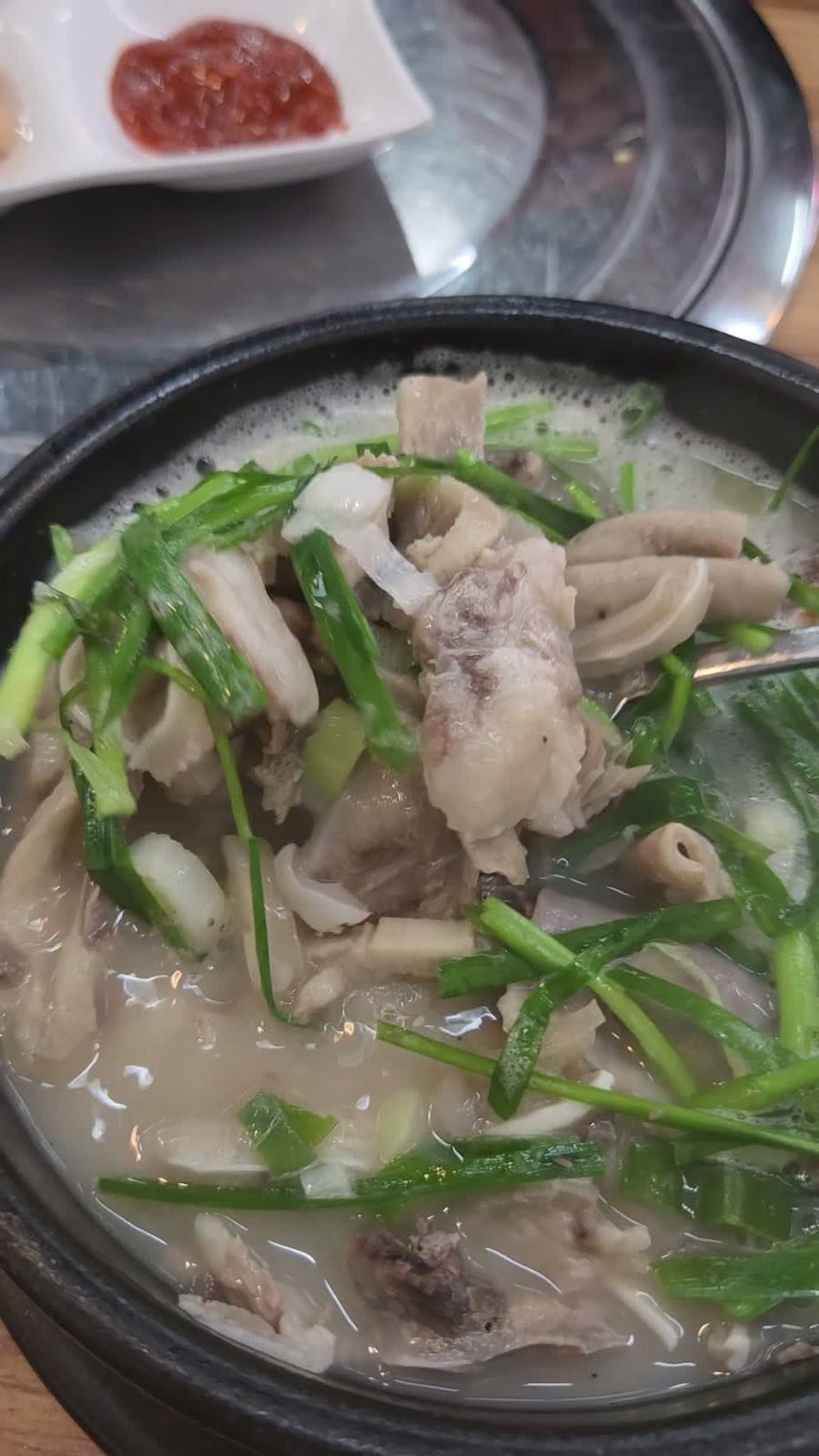 Black stone bowl of milky pork broth topped with garlic chives, sliced pork and offal