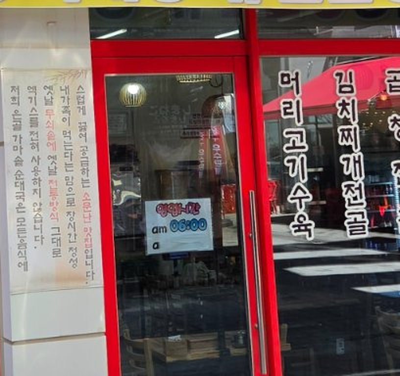 Hand written sign taped inside a red framed glass door reading 영업시간 am 06:00