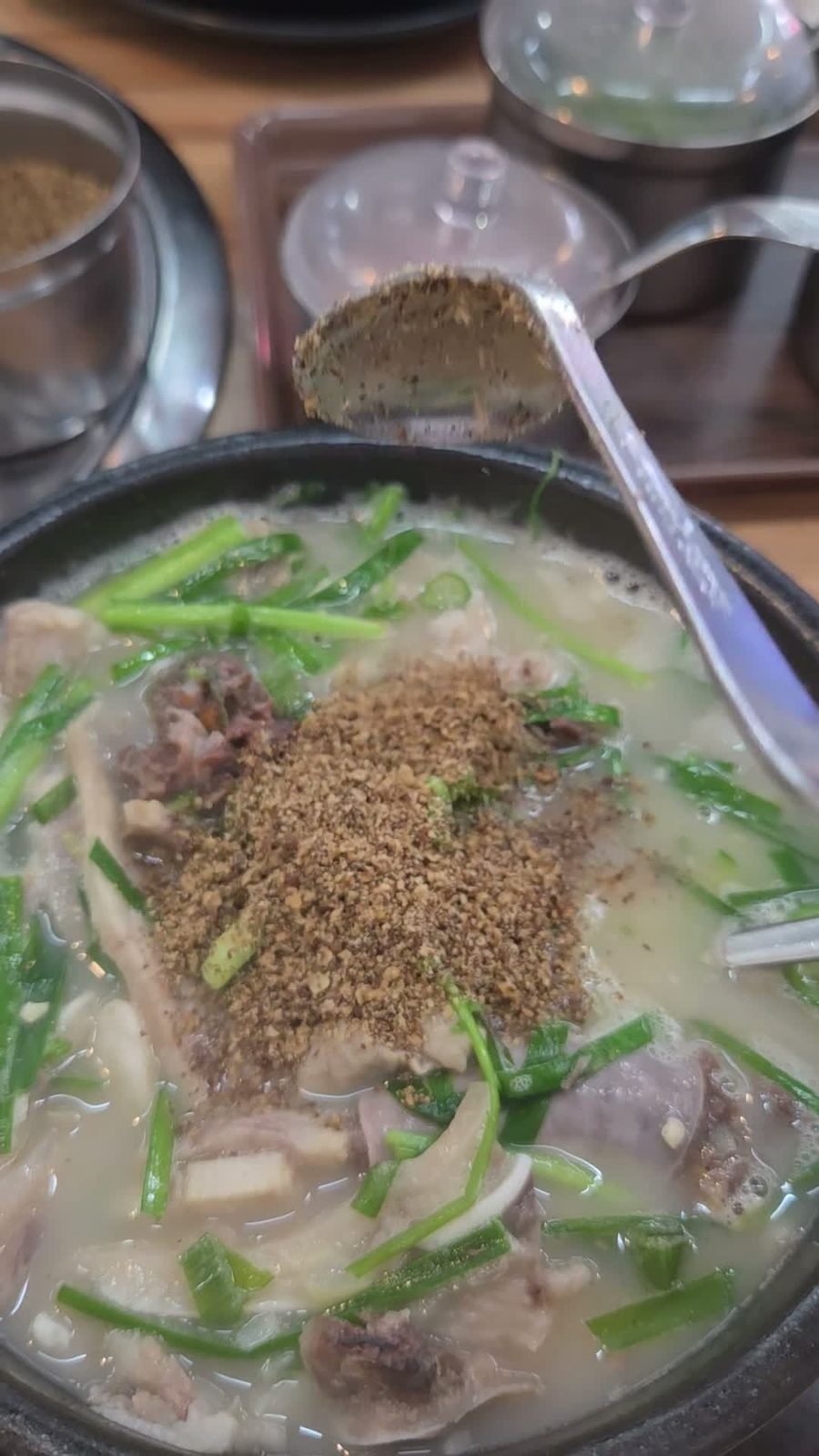 A spoonful of ground perilla seed tipped onto the surface of a milky pork soup