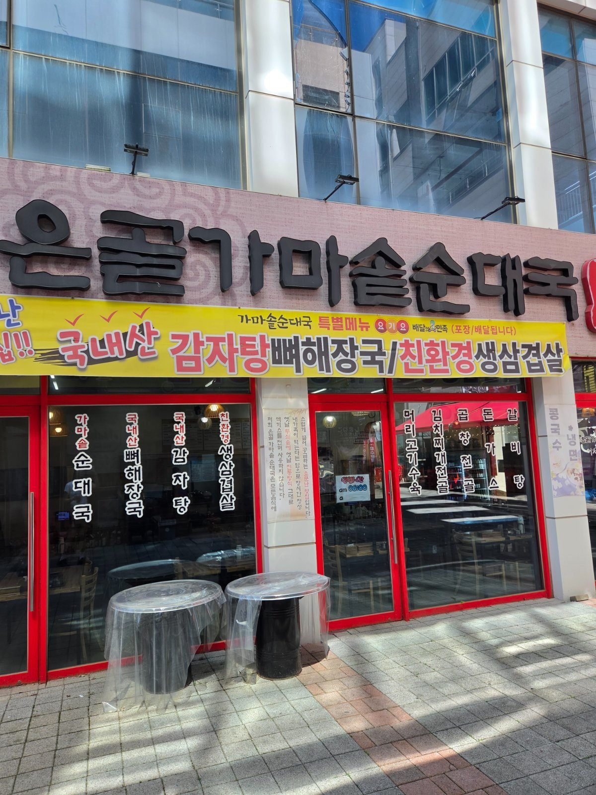 Red framed glass shopfront under a large black Korean sign, with a yellow banner advertising pork bone stew and grilled pork belly