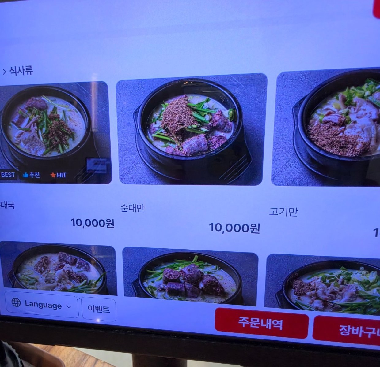 Self order tablet screen showing three pork soup dishes at 10,000 won each, with a globe icon labelled Language at the bottom left