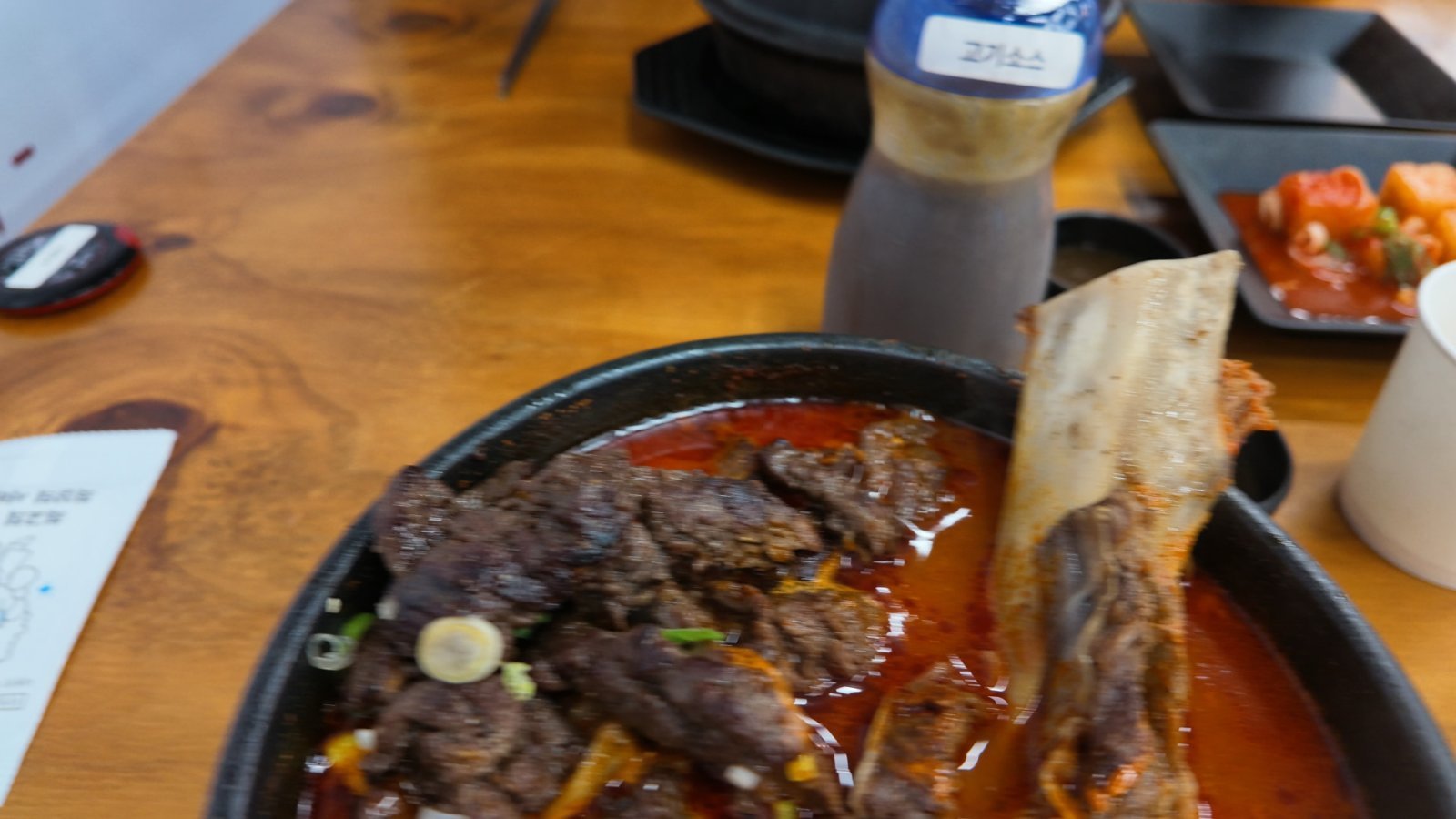 Cast-iron pot of singaltang, a deep red spicy short-rib soup with grilled beef and spring onion on top and a large rib bone propped against the rim
