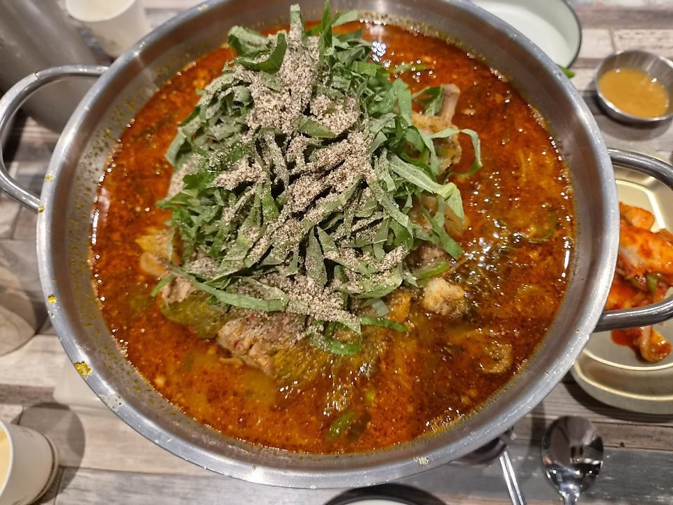 A pot of gamjatang at Chamdeul Ppyeogui Gamjatang, pork spine in red broth under a heap of perilla leaves and perilla seed powder.