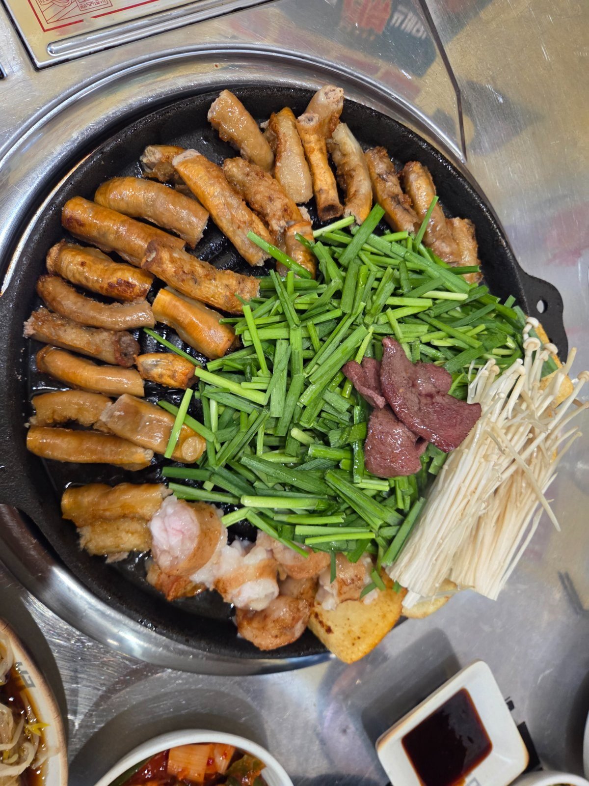 Raw gopchang laid in a ring on a round black griddle with chopped chives, enoki mushrooms and dark red slices of liver piled in the centre
