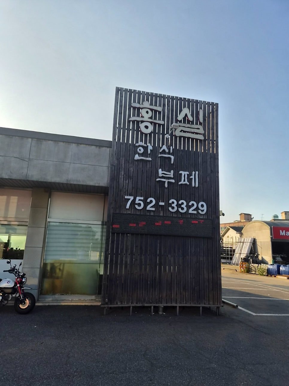 Black wooden signboard reading Hongsil Korean buffet in Korean with the phone number 752-3329, on a low building in Unnam-dong, Yeongjong Island.