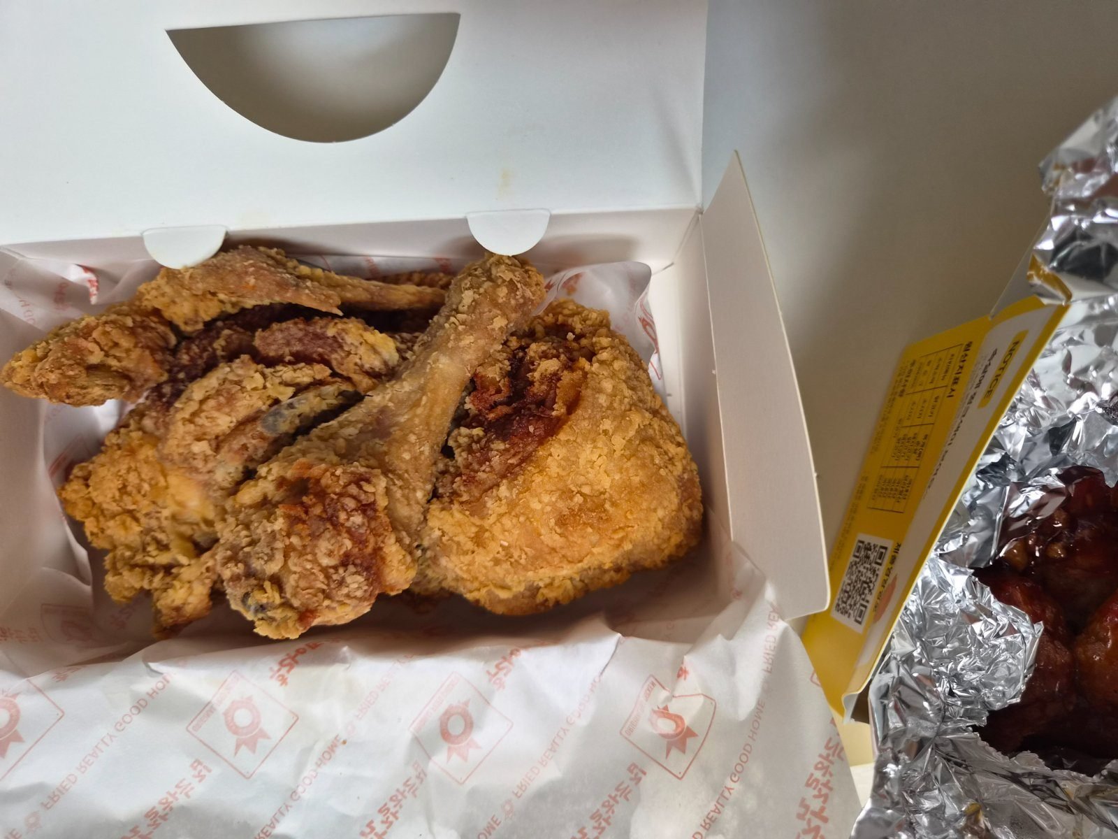 Plain Korean fried chicken pieces, mostly drumsticks and wings, in an open paper box with a pickled radish tub