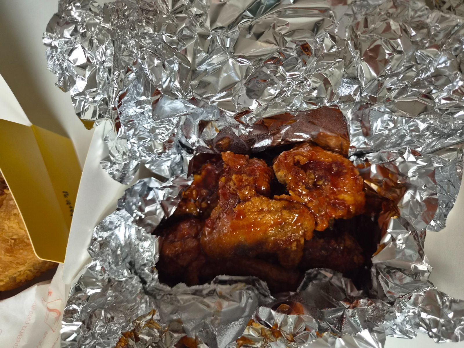 Red glazed Korean seasoned chicken pieces in an open foil wrap