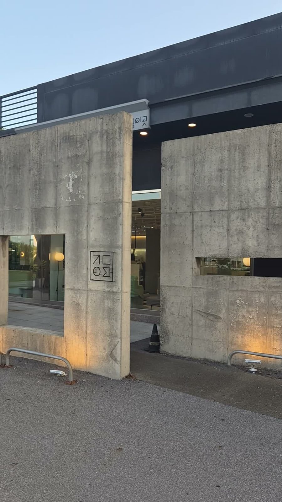 Exposed concrete exterior of Jigeum-i-got bakery cafe at dusk with a lit entrance