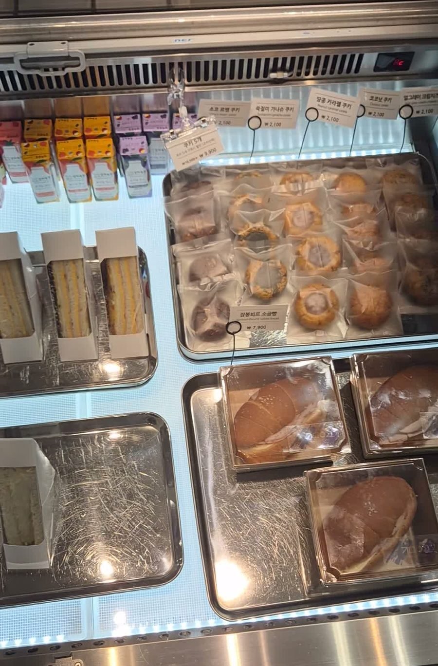 Bakery display case with individually wrapped cookies, sandwiches and packaged jambon-beurre salt bread under bilingual price tags