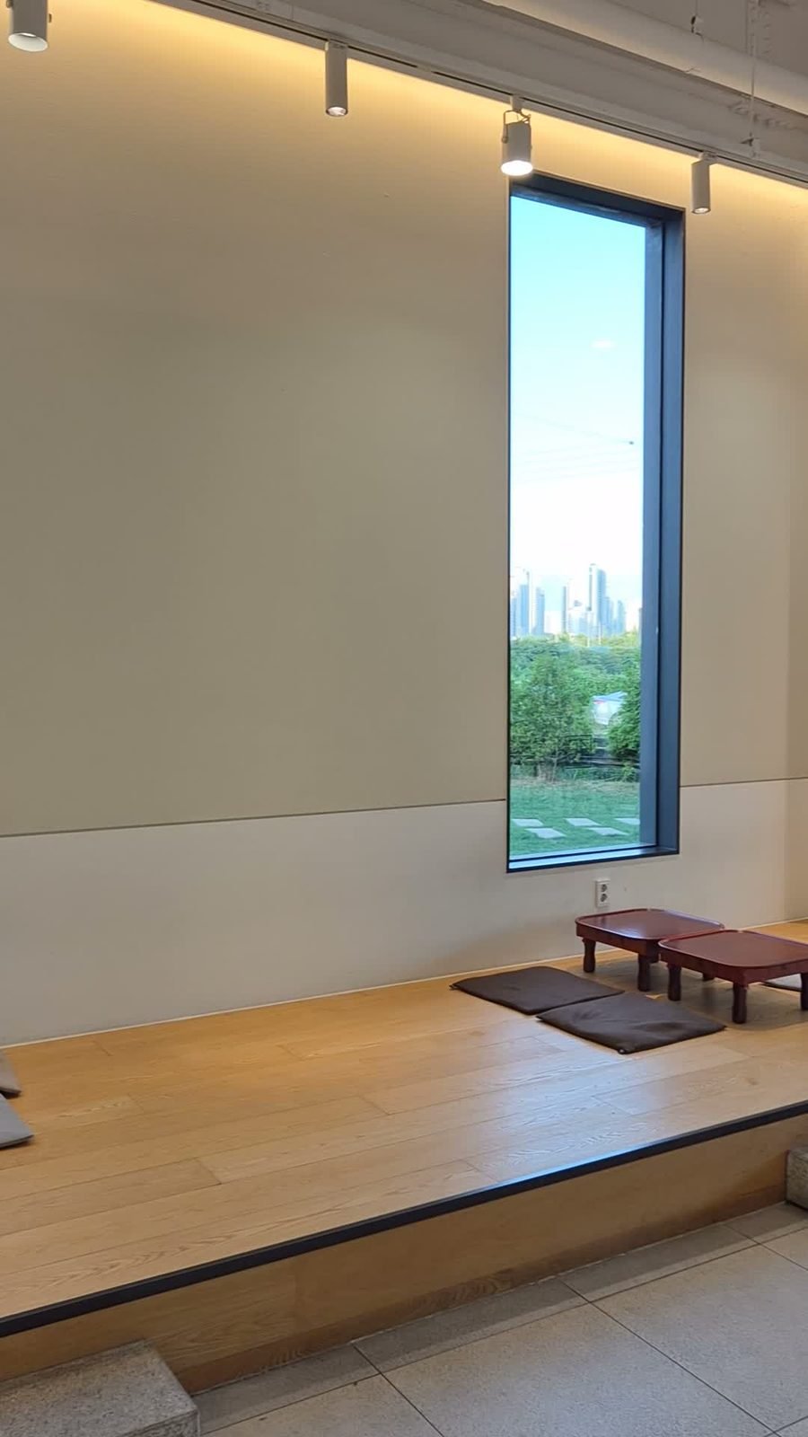 Raised wooden floor seating platform with cushions and a tall window showing a distant skyline