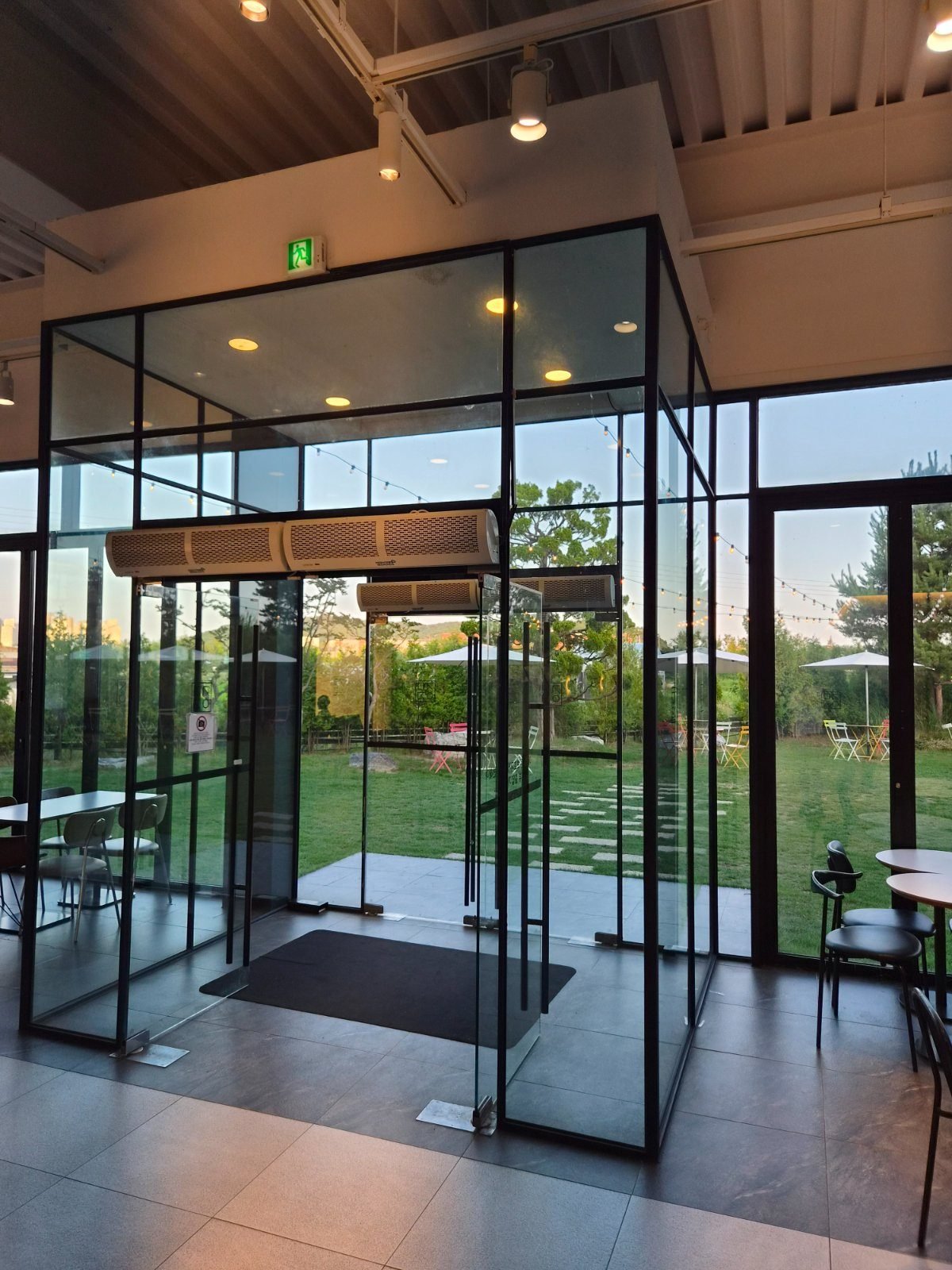 Glass vestibule doors inside the cafe opening onto a lawn with parasols