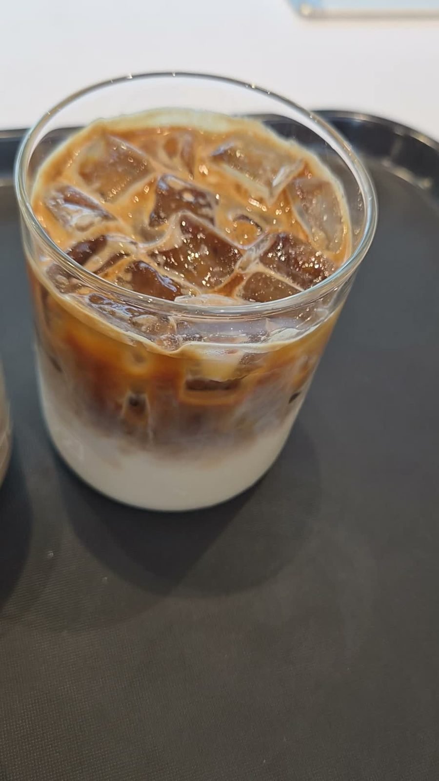 Layered iced latte in a glass tumbler on a dark tray