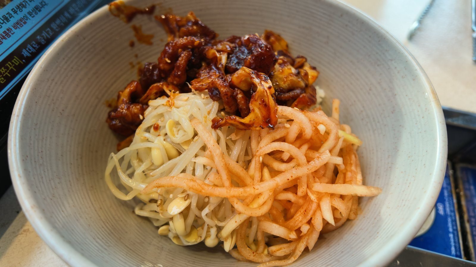 A shallow bowl of red-sauced grilled baby octopus piled next to bean sprouts and shredded seasoned radish.