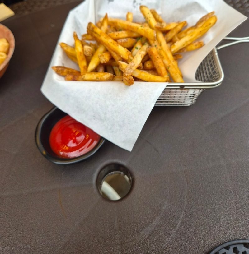 A metal fry basket of seasoned chips on greaseproof paper with a dish of ketchup, on the terrace table at Kim Boknam Beer