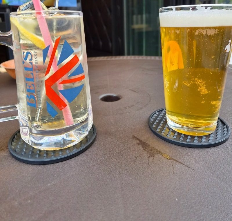 A lemon highball in a Bell's glass mug with a pink straw next to a glass of pale draft beer with a thick white head, on rubber coasters